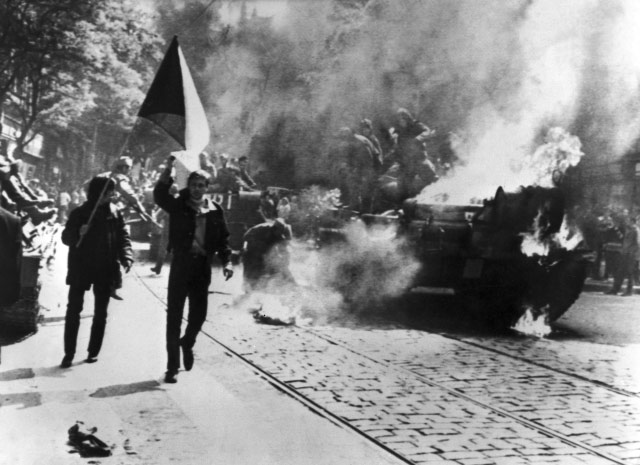Czechoslovaks carry their national flag past a burning Soviet tank in Prague.