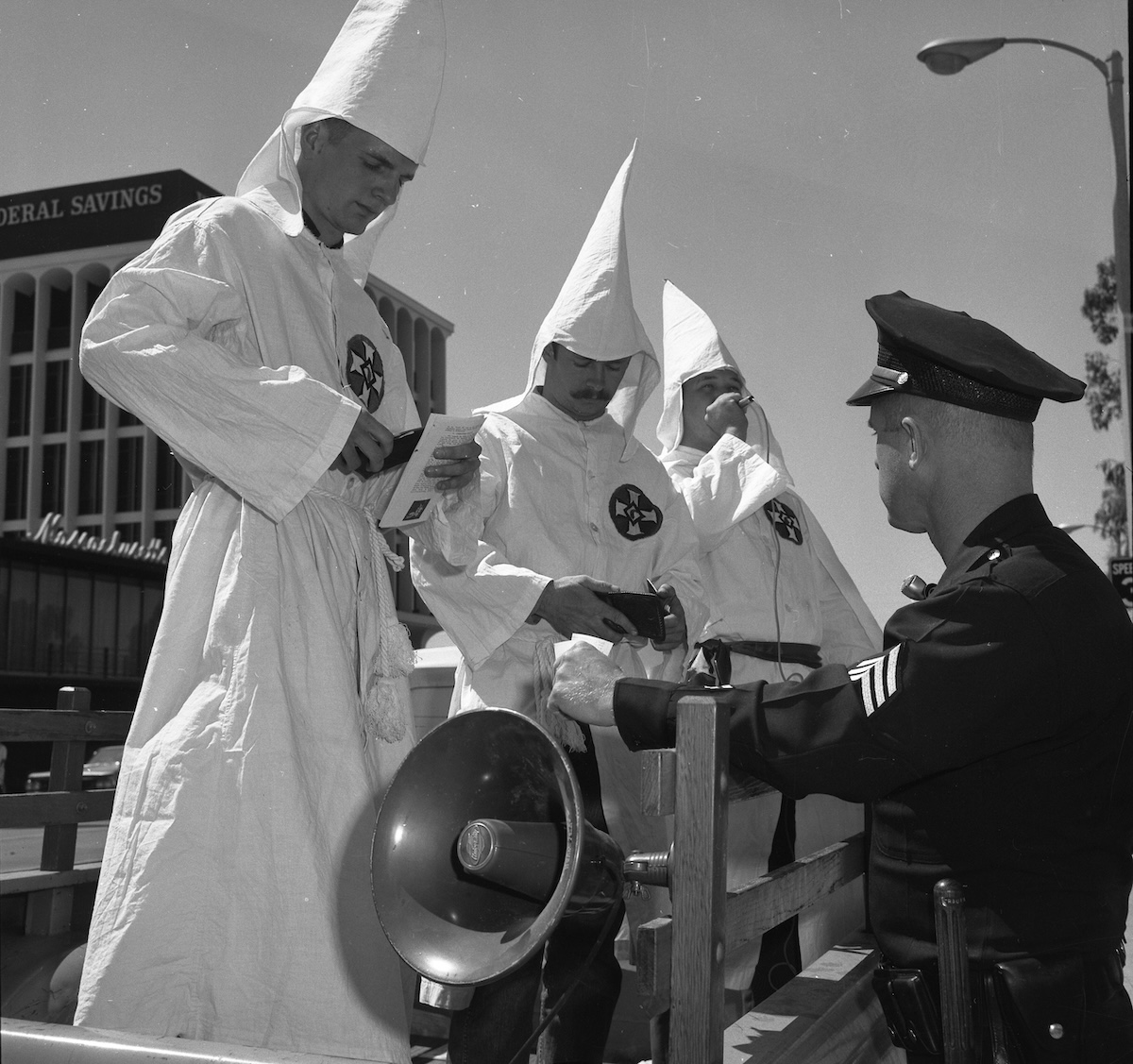 A police officer checks the ID of three members of the Ku Klux Klan in Panorama City, California, 18 September 1966. University of California, Los Angeles. Library. Department of Special Collections (CC BY 4.0).