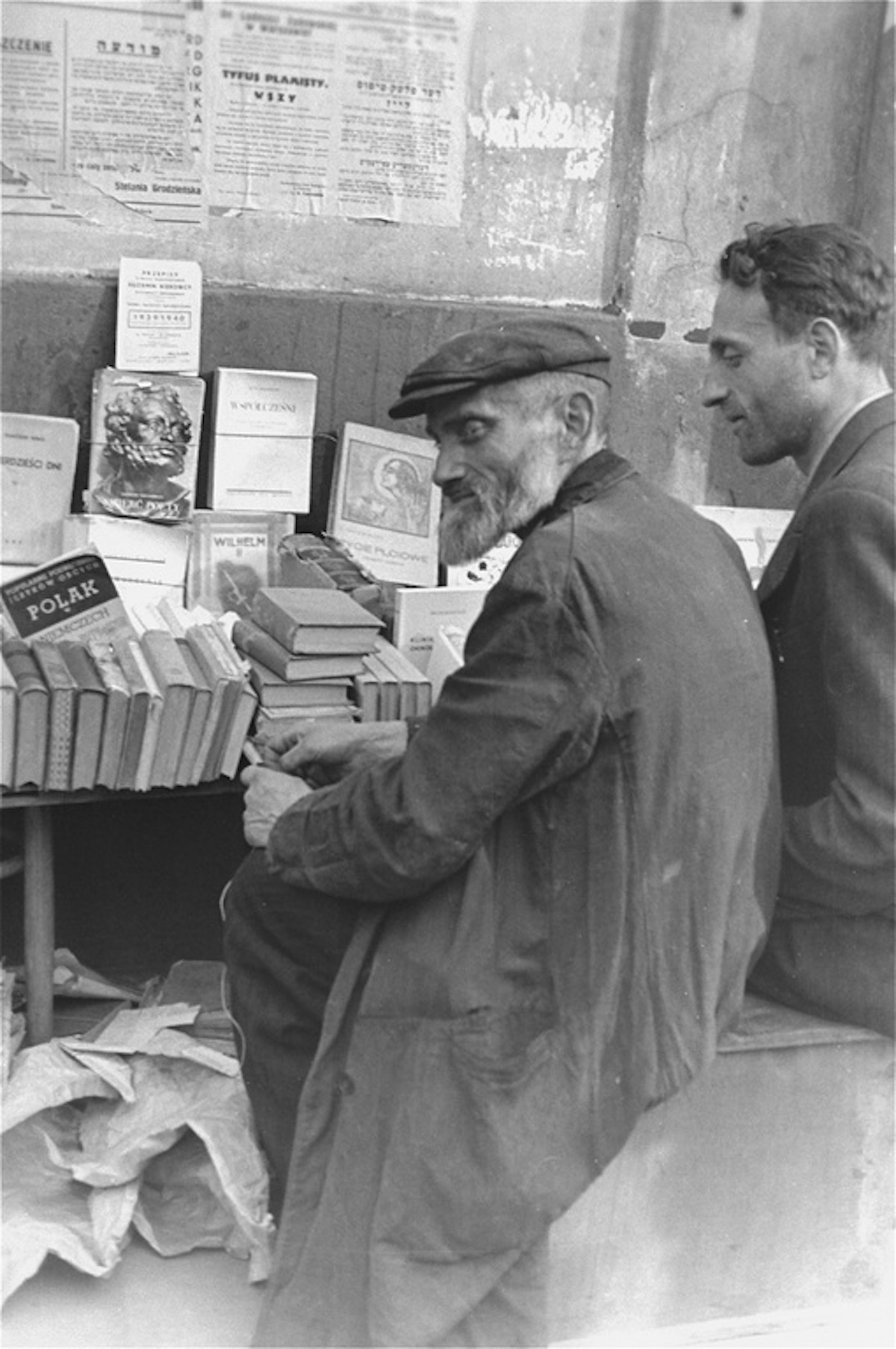 Book vendors sit in front of a table piled with books on a street in the Warsaw ghetto., c. June-August 1941. United States Holocaust Memorial Museum, courtesy of Rafael Scharf.