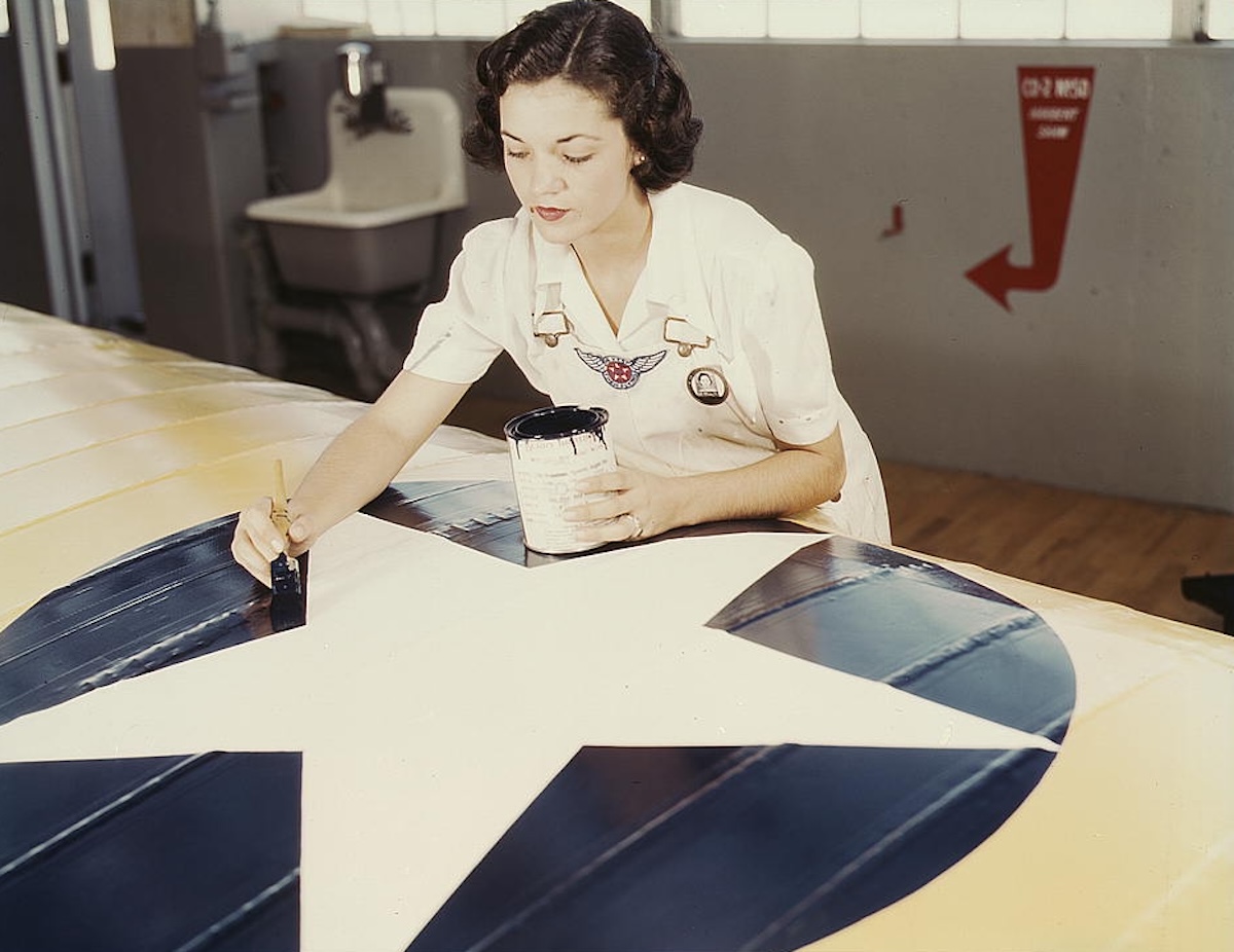 A woman paints an insignia on the wing of a US Navy plane, August 1942. Library of Congress. Public Domain.