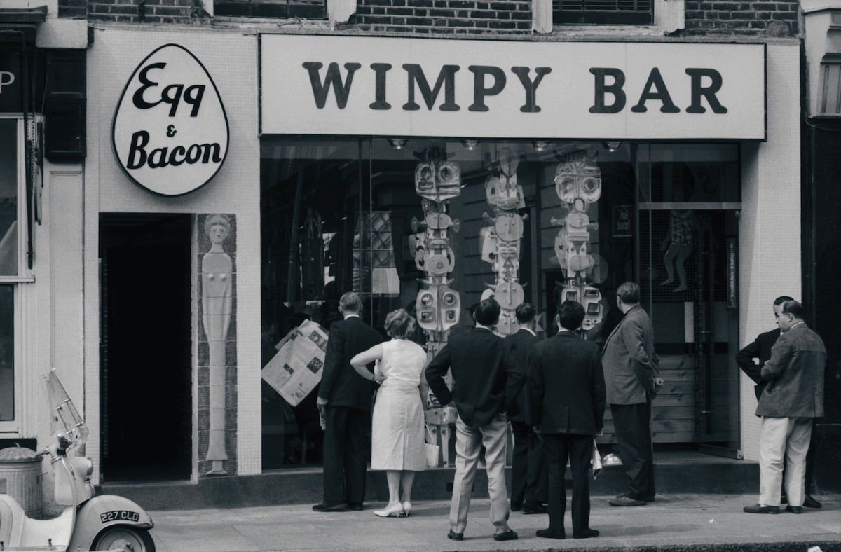 Passers-by looking at a modern sculpture in the window of a Wimpy Bar in London, c.1961. Photograph by John ‘Hoppy’ Hopkins. © Estate of John Hopkins. Passers-by looking at a modern sculpture in the window of a Wimpy Bar in London, c.1961. Photograph by John ‘Hoppy’ Hopkins. © Estate of John Hopkins.