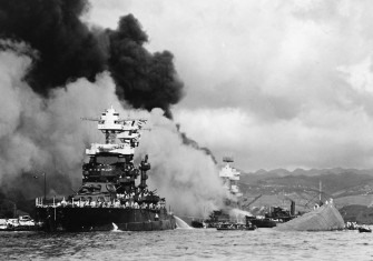 The U.S. Navy battleship USS Maryland (BB-46) alongside the capsized USS Oklahoma (BB-37) at Pearl Harbor. The USS West Virginia (BB-48) is burning in the background.